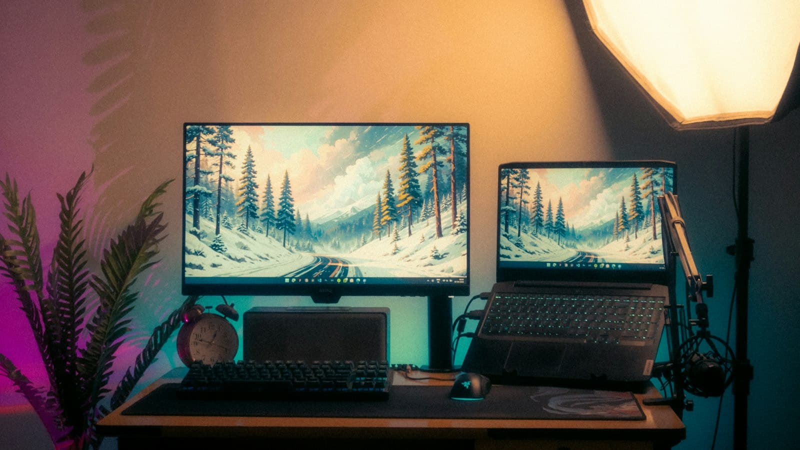 A desk setup with a monitor, a laptop, a keyboard and a studio light